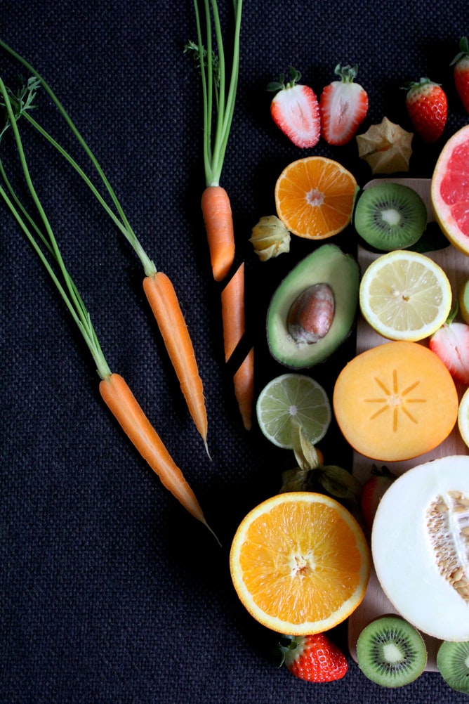Colorful sliced fruits including kiwi, citrus, and strawberries on a dark cloth backdrop